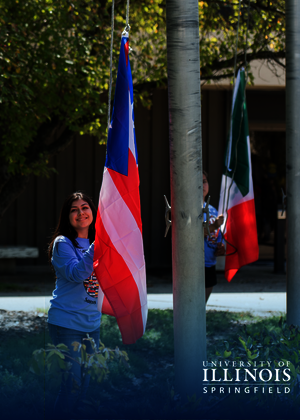 Two people raise flags outdoors in front of a building.