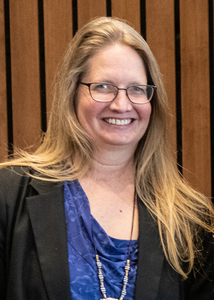 Smiling woman with long hair, wearing glasses and a blue top.