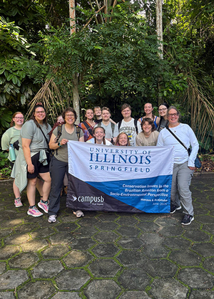 Group of people holding a University of Illinois Springfield banner in a lush, green setting.