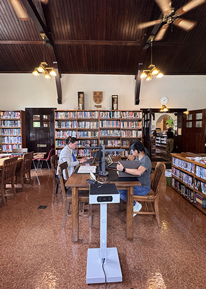 Cozy library with two people working at a wooden table, surrounded by bookshelves.