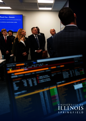 People in business attire attending a presentation, with financial data on screens.
