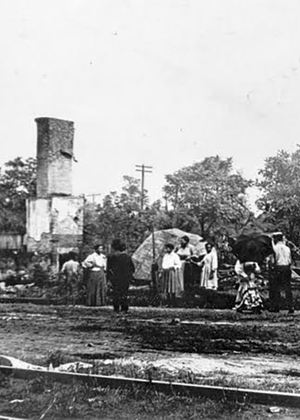 People standing near a tall, damaged building with trees in the background.