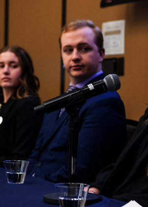 Panel of six people sitting at a table, one speaking into a microphone.