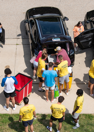 People unloading cars, wearing yellow shirts, outdoor setting.