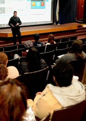 Audience listens to a presentation from police officers in an auditorium setting.