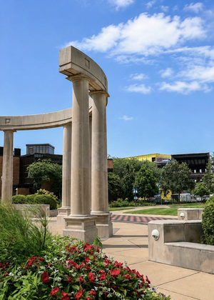 Stone columns in a sunny garden with blue sky and clouds.