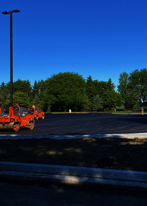 Paved parking lot under clear blue sky, surrounded by trees, with orange construction cones.