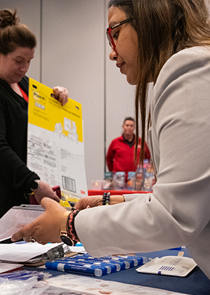 Two people interacting at a busy indoor booth, exchanging documents.