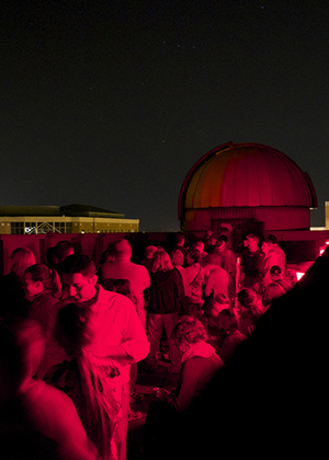 Crowd under red lighting at night, with dome in the background.