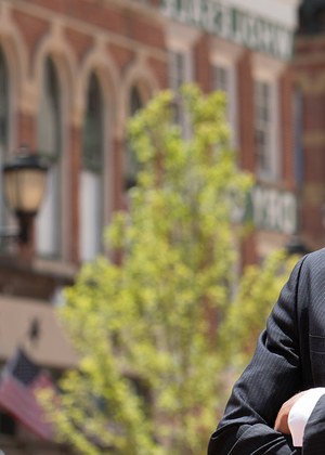 Professional person in a suit smiling, standing with arms crossed in a historic street.