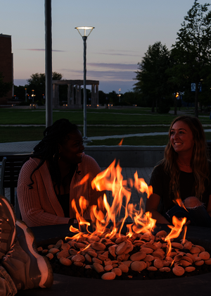 People gathered around a fire pit at dusk, smiling and talking.