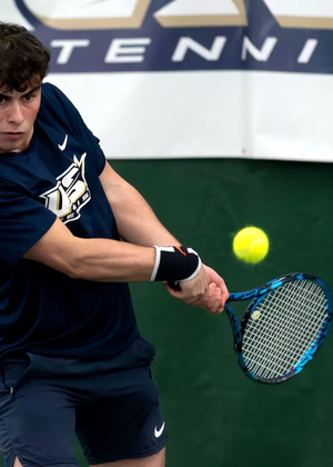 Pablo Herrera playing tennis indoors in blue UIS Uniform