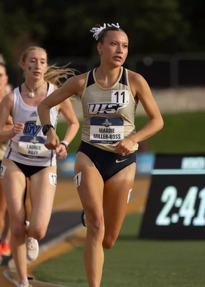 Maddie Miller-Ross running an outdoor track race in gold UIS uniform