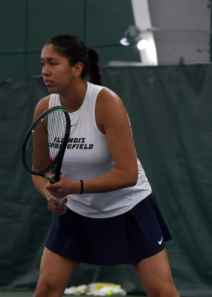 Cristina Mendoza Romero playing tennis in blue and white UIS uniform
