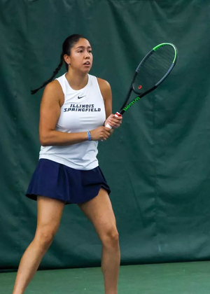 Cristina Mendoza Romero playing tennis indoors in white and blue UIS uniform