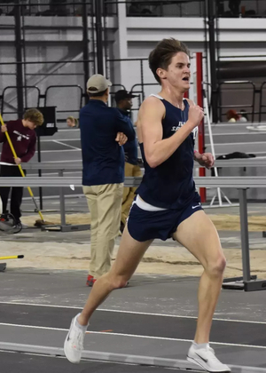 Ryan Kries running at an indoor track in blue UIS uniform
