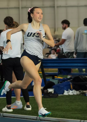 Madelyn Miller-Ross running indoor track in white UIS uniform