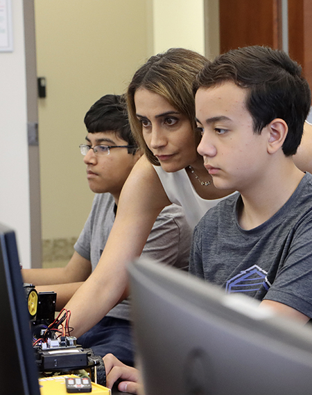 Elham Buxton (center) is shown reaching past a student to control a computer during an AI summer camp.