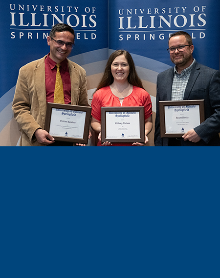 Three faculty members stand holding awards.