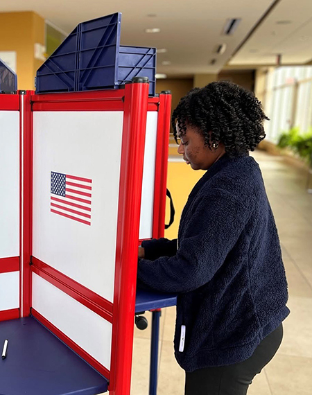 Student casts ballot at a red, white and blue voting booth inside the University of Illinois Springfield student union.