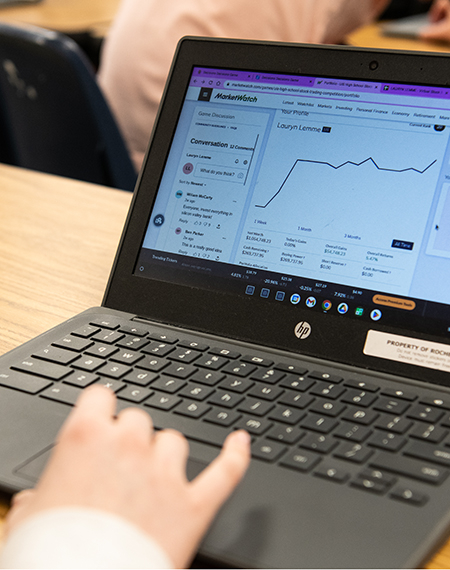A laptop with stock trading information on the screen sitting on a desk with a person's hand above the mousepad. 