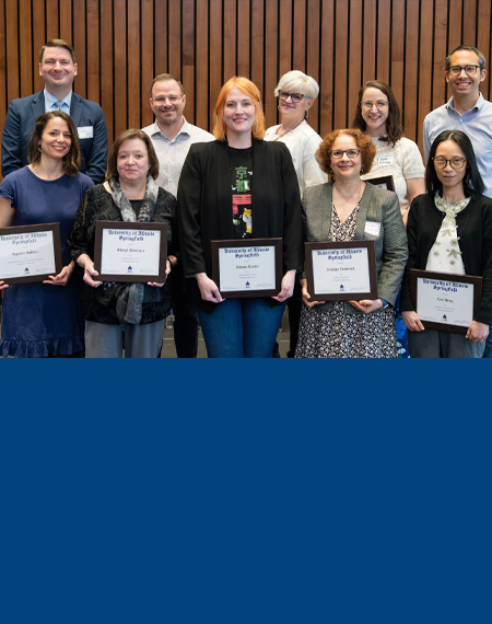 Ten faculty members pose for a photo holding their awards. 