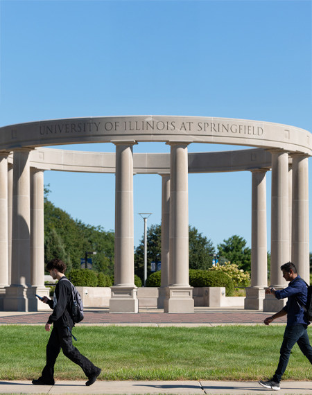 Two students walk in front of the UIS colonnade on a sunny day.