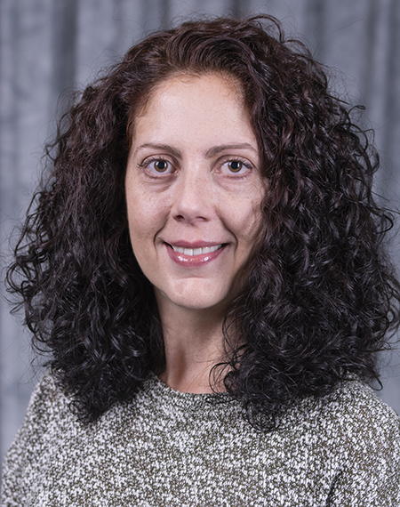 Smiling woman with curly hair against a gray backdrop.