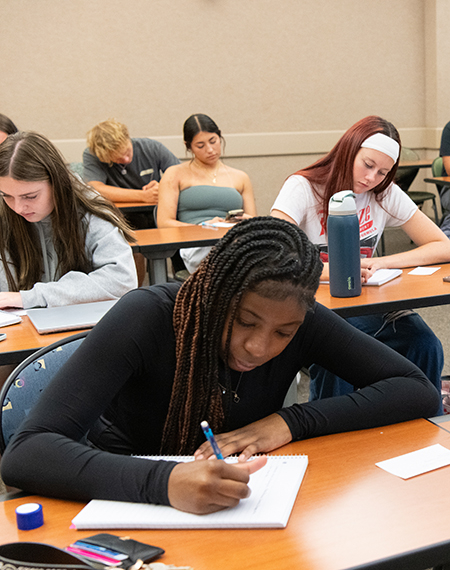 Students focused on writing at desks in a classroom.