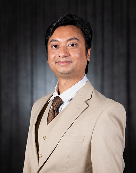 Man in a tan suit with a tie, black background, smiling gently.