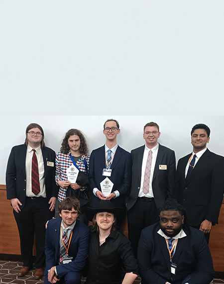 Eight people in formal attire, two holding awards, smiling indoors.
