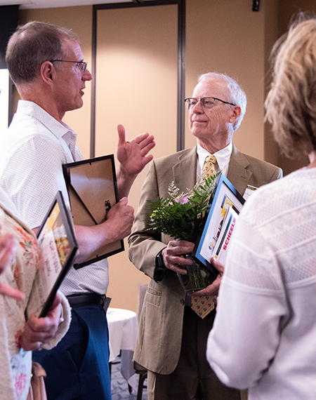 Two men in discussion at an event, holding framed certificates.