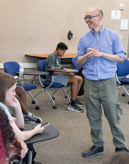 Man in blue shirt speaking to students in a classroom setting.