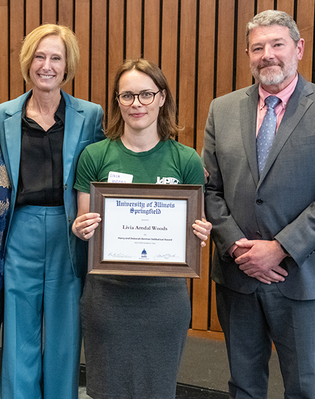 Three people standing, one holding a framed certificate.