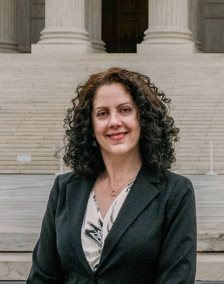Woman in a suit smiling in front of a building with large steps.