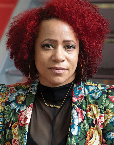 A woman with curly red hair, wearing a floral jacket and hoop earrings.