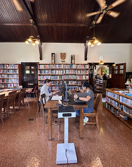 Cozy library with two people working at a wooden table, surrounded by bookshelves.