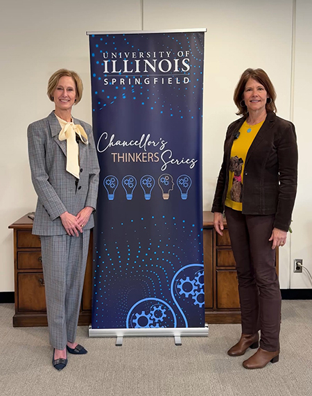 Two women standing beside University of Illinois Springfield banner indoors.