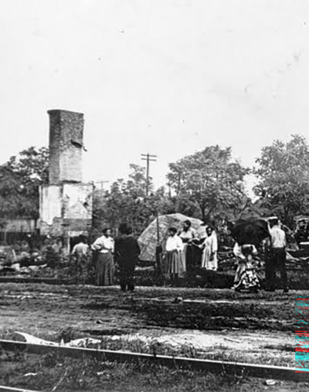 People standing near a tall, damaged building with trees in the background.