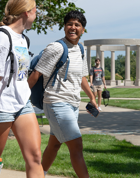 Students smiling, walking on grassy campus with backpacks.