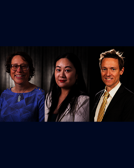 Three people in formal attire, smiling in a dark studio setting.