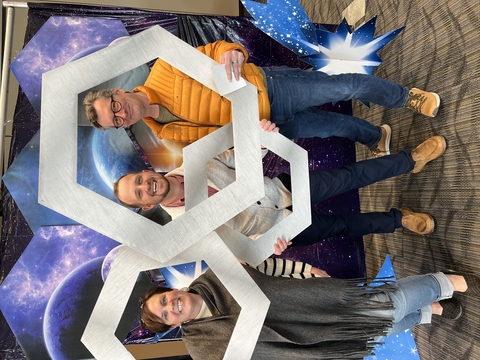 Three people holding photo props shaped as hexagons. 