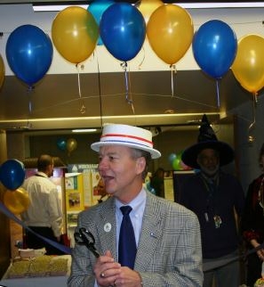 A man wearing a hat holding a pair of scissors while standing in front of a ribbon.