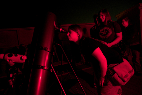 a person looks through a telescope with other people waiting to do the same