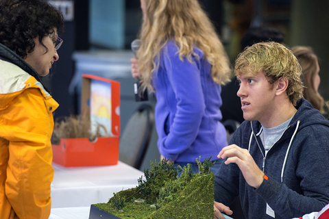 a student explaining their research and model to an audience member