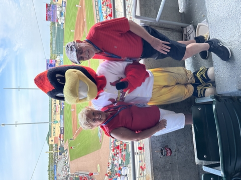 two people pose with a Redbird mascot in front of a baseball field