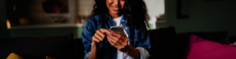 A smiling woman using her smartphone while sitting on a couch
