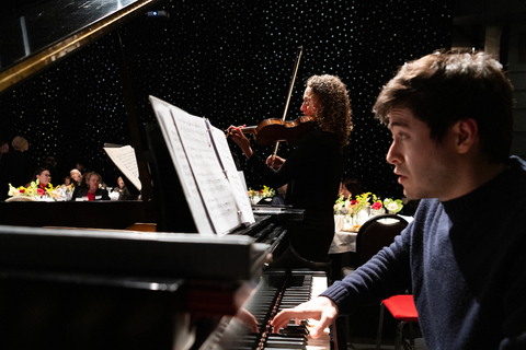 a man plays a piano with a woman playing the violin in the background