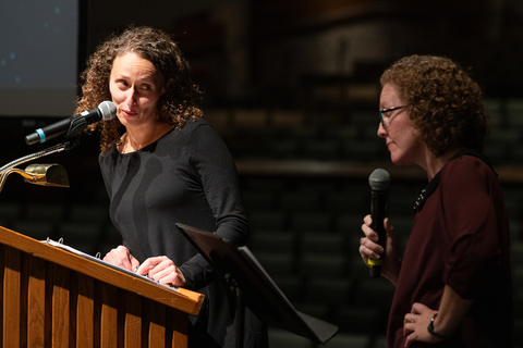 Two speakers look at each other during a presentation