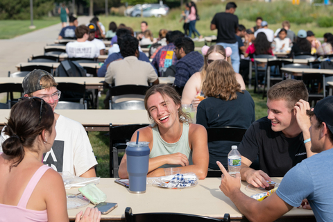 Students sitting at picnic tables outside.